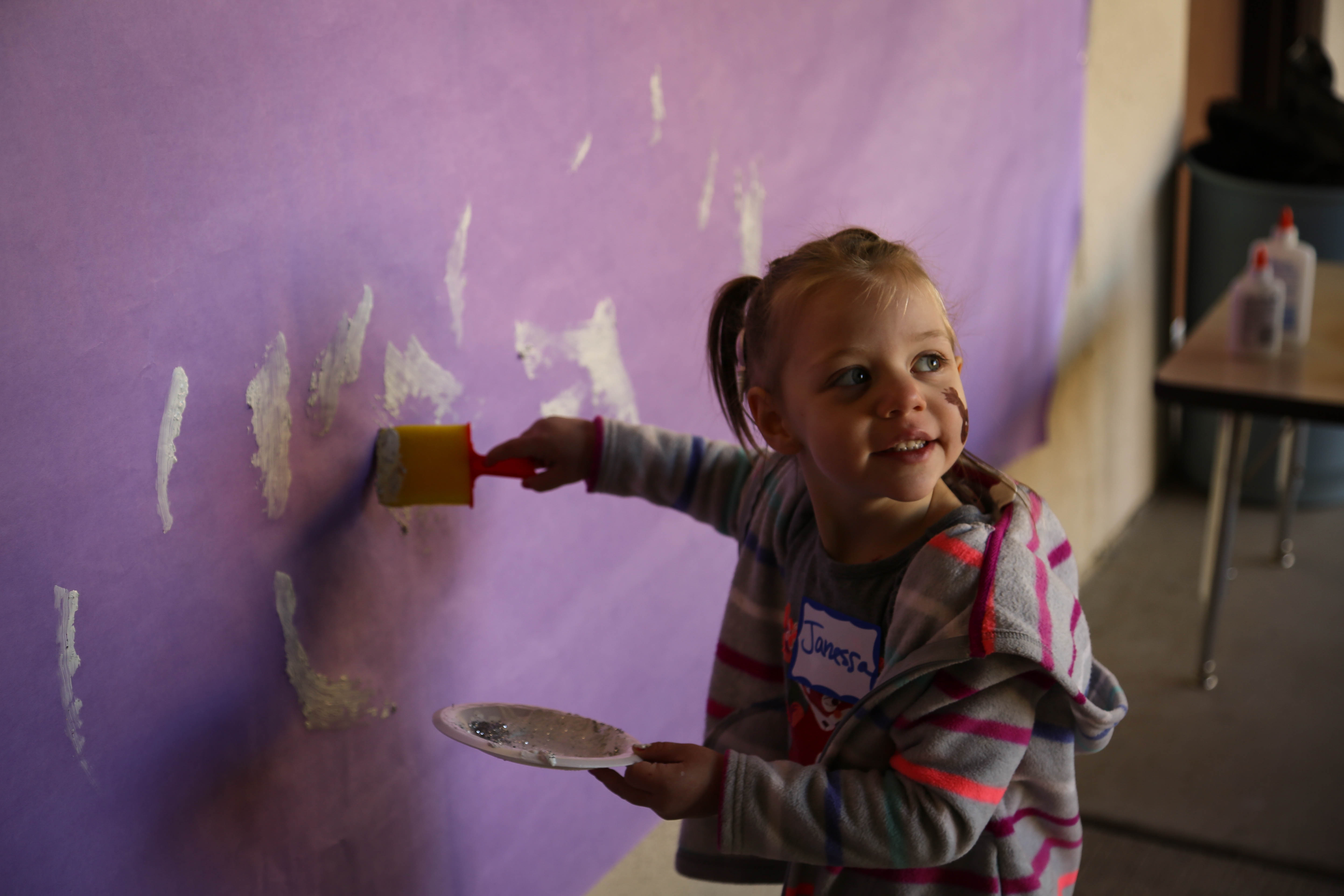 Child with paint on face drawing on wall