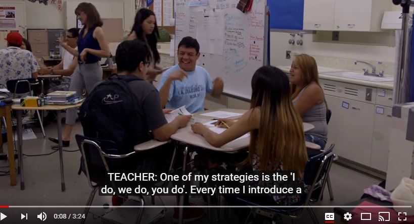Video capture of four students working together while sitting at a large desk
