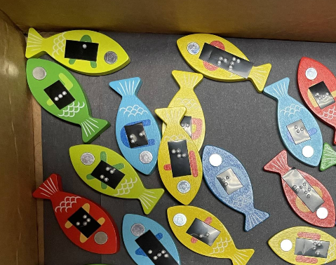 box of cut out fish with braille letters on them.