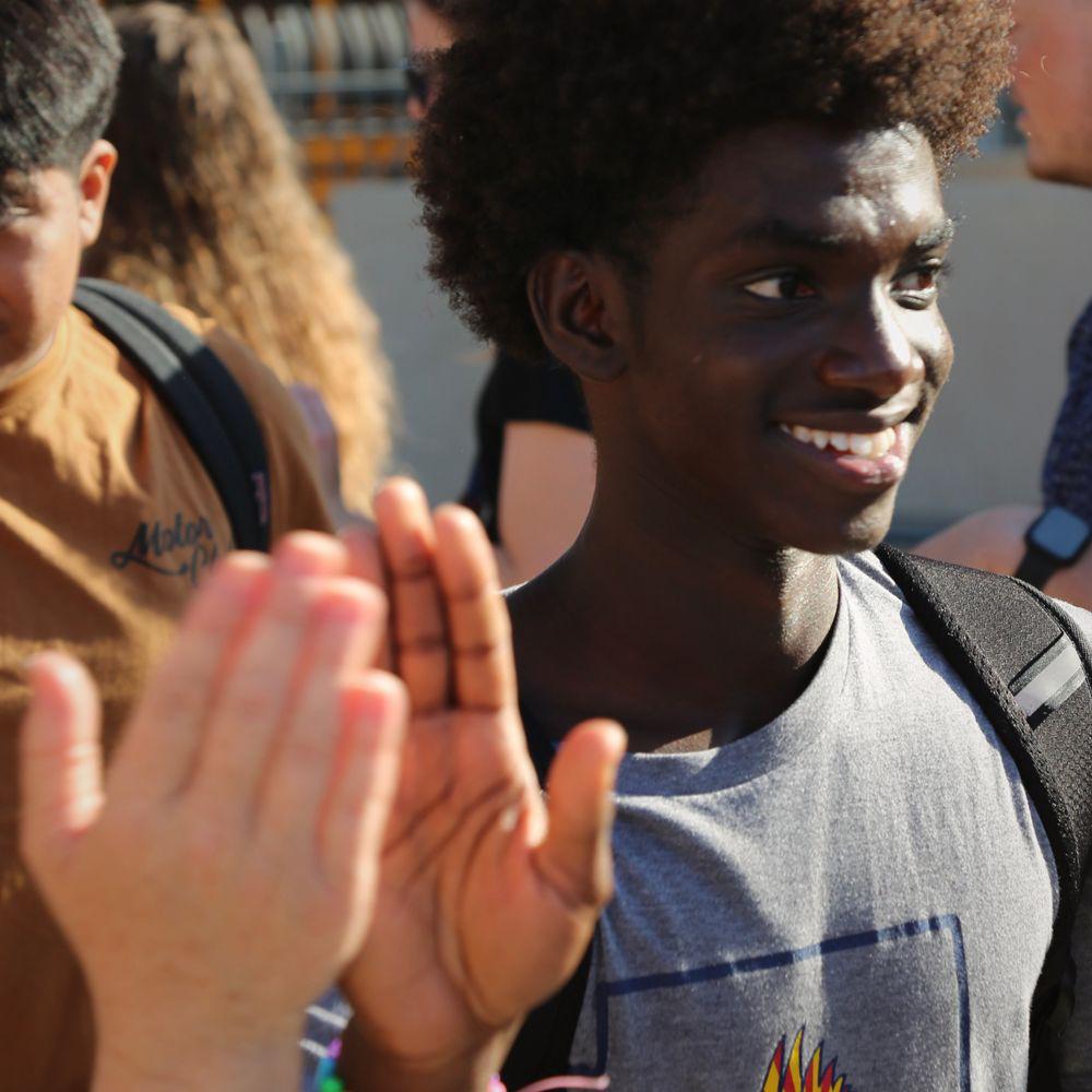 A young sophomore smile as he high fives teachers.