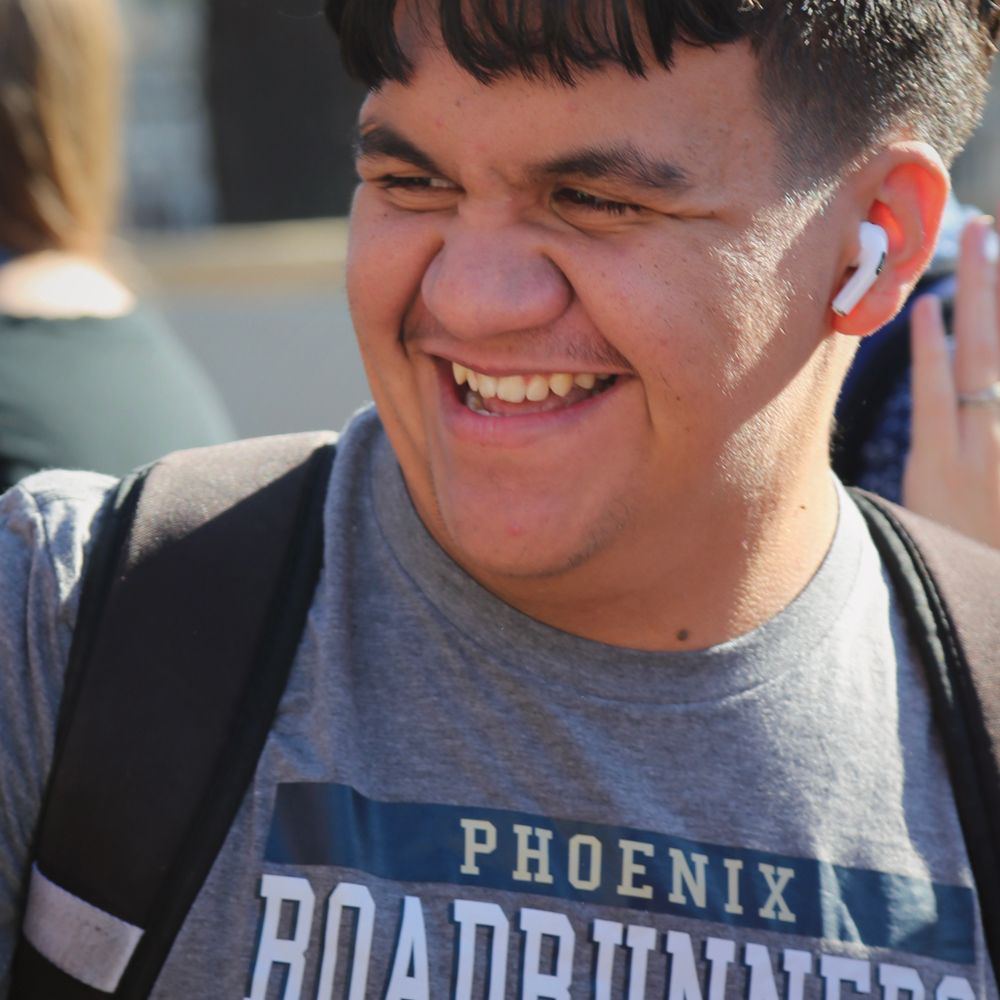 A male student wearing a Phoenix Roadrunners t-shirt is very happy as he smiles at his teacher.