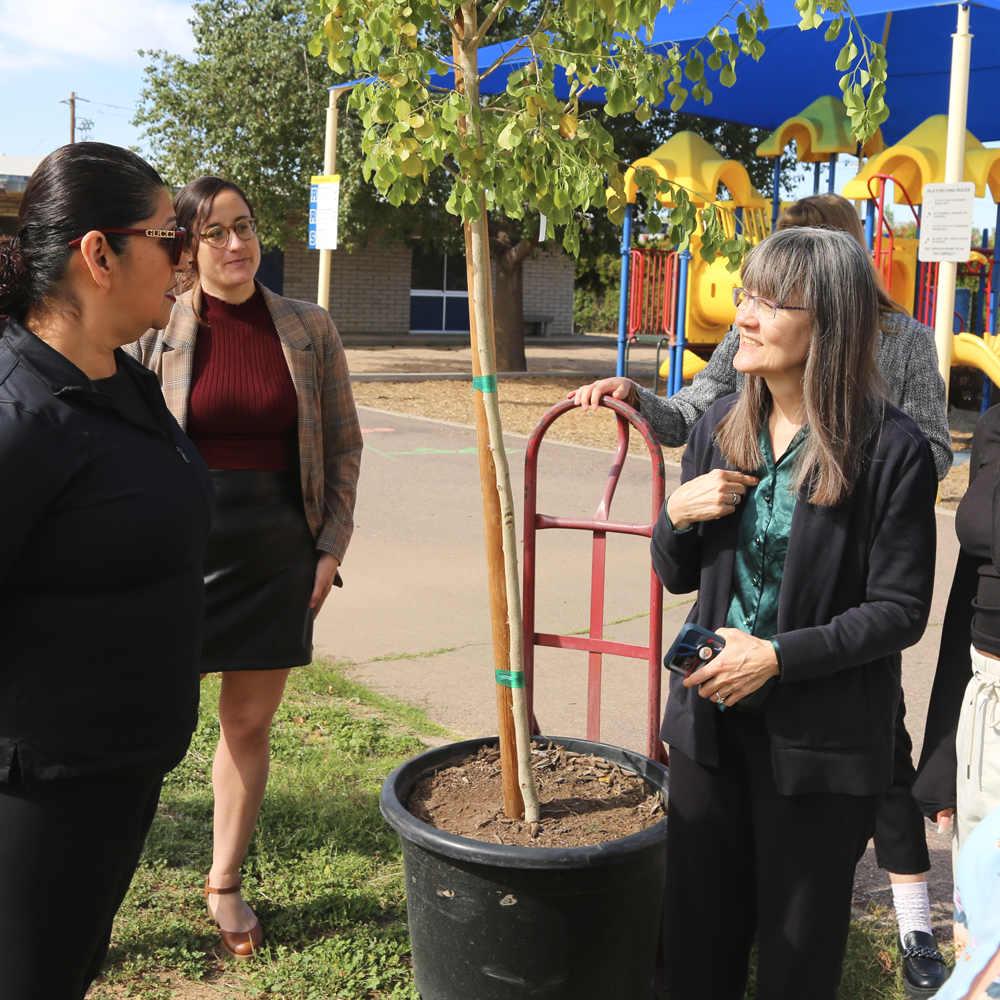 Annette Reichman chats with Councilwoman Betty Guardado with Shelley Beaudean looking on. They are standing next to the first tree to be planted as Annette invites Betty to return whenever she'd like for a full tour of the campus.