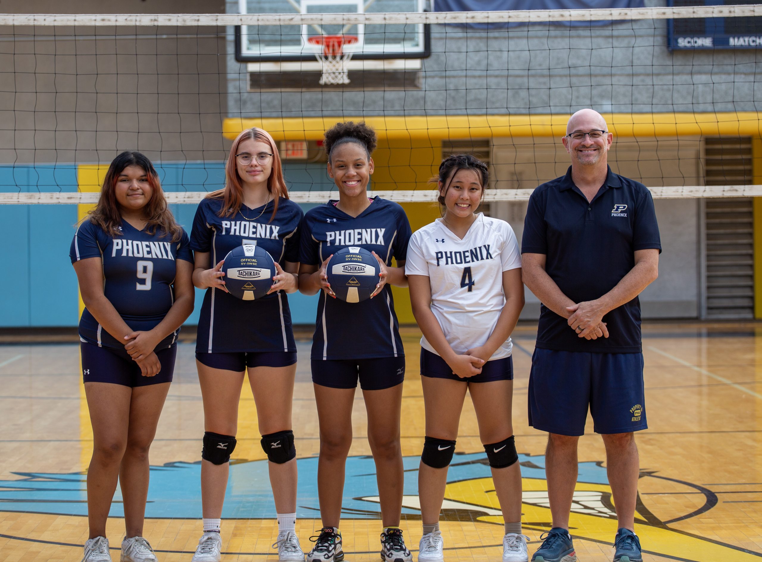 An image of four HS volleyball players and the coach posing for a photo.