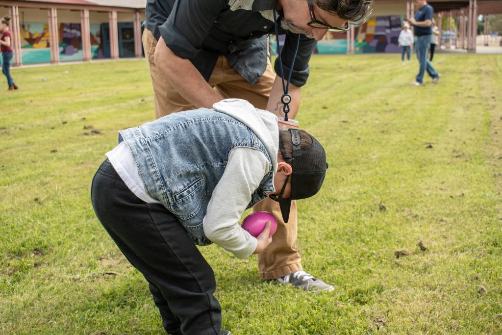 A student bends down to inspect a pink egg with a staff member