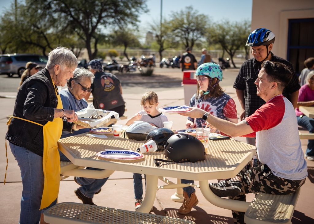 A volunteer from Oro Valley Lion's Club passes out breakfast sausage links to a group of dorm students.