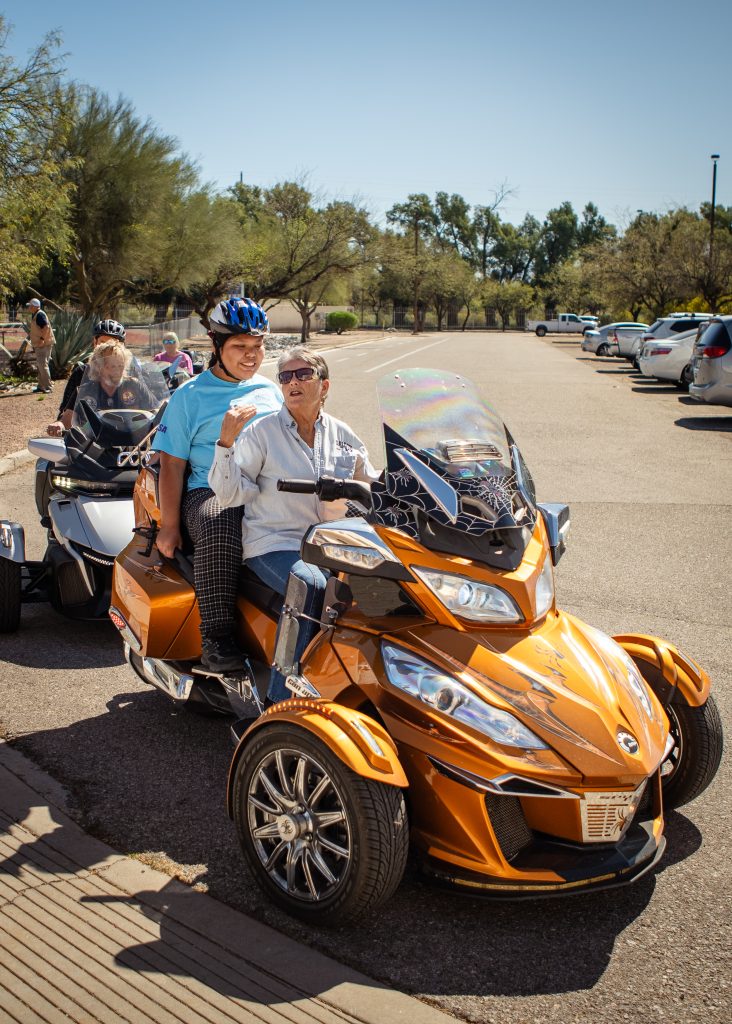 A blind student smiles as they start their ride on an orange motorcyle.