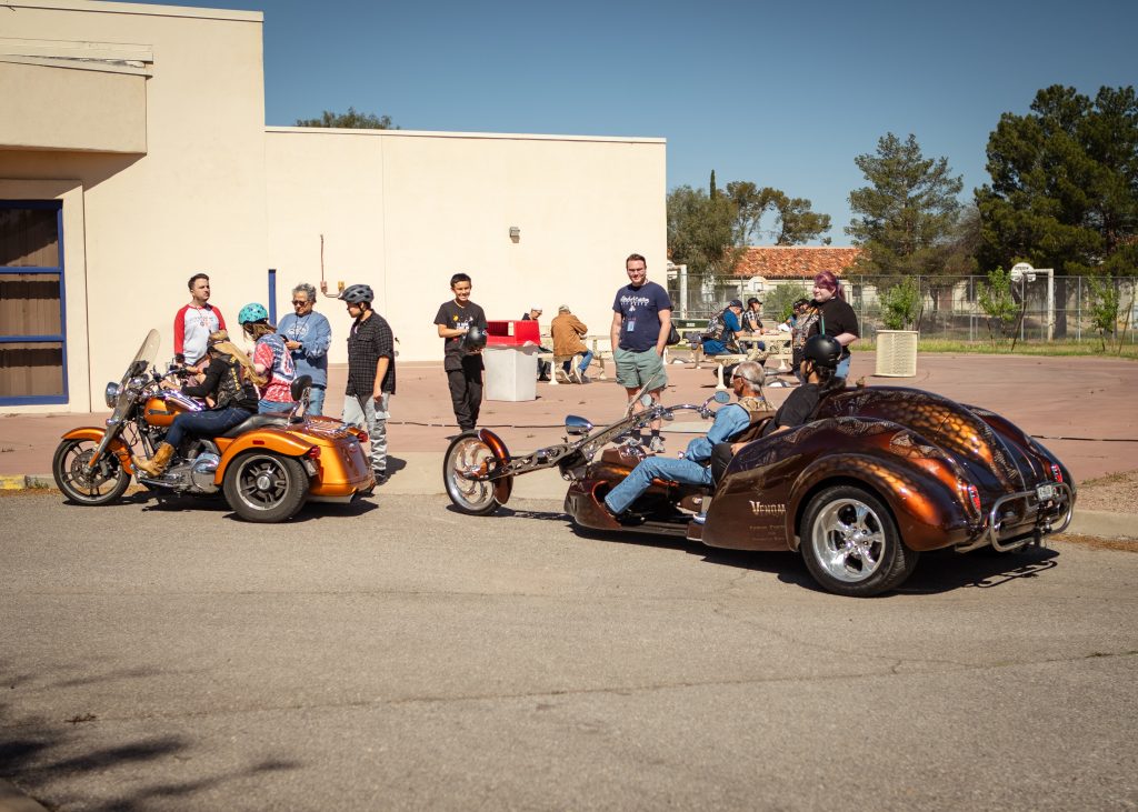 a photo showing 2 motorcycles, the students getting on to ride in front of the gym.