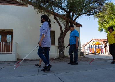A photo of four visually impaired students walking through a corridor on ASDB campus. Each of them is using a white cane to help themselves navigate.