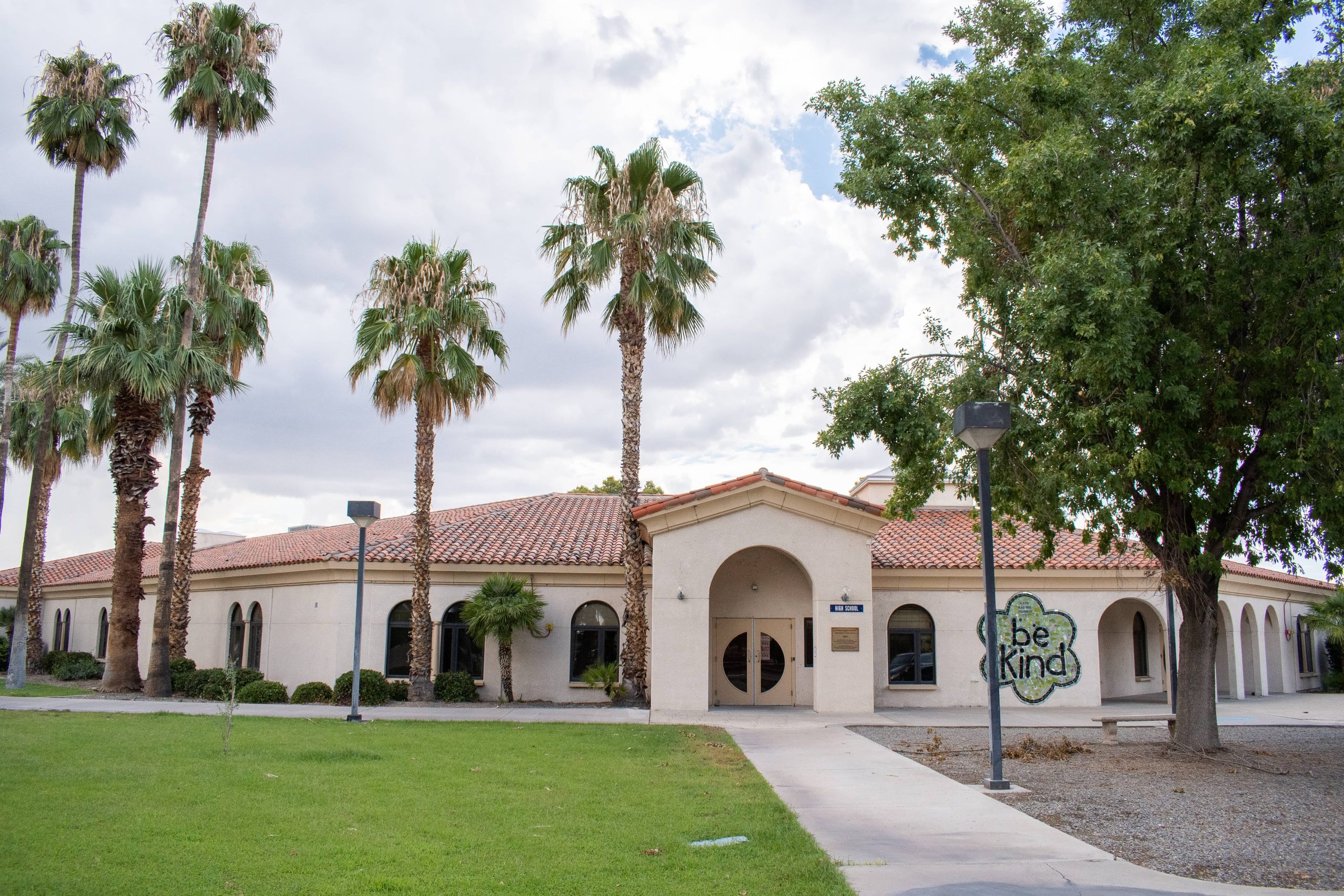 A panoramic photo of the high school building on ASDB campus. The building has beige, stucco walls, large, arched windows, a Spanish-tiled roof, and a tiled mural which reads, 'Be Kind'.