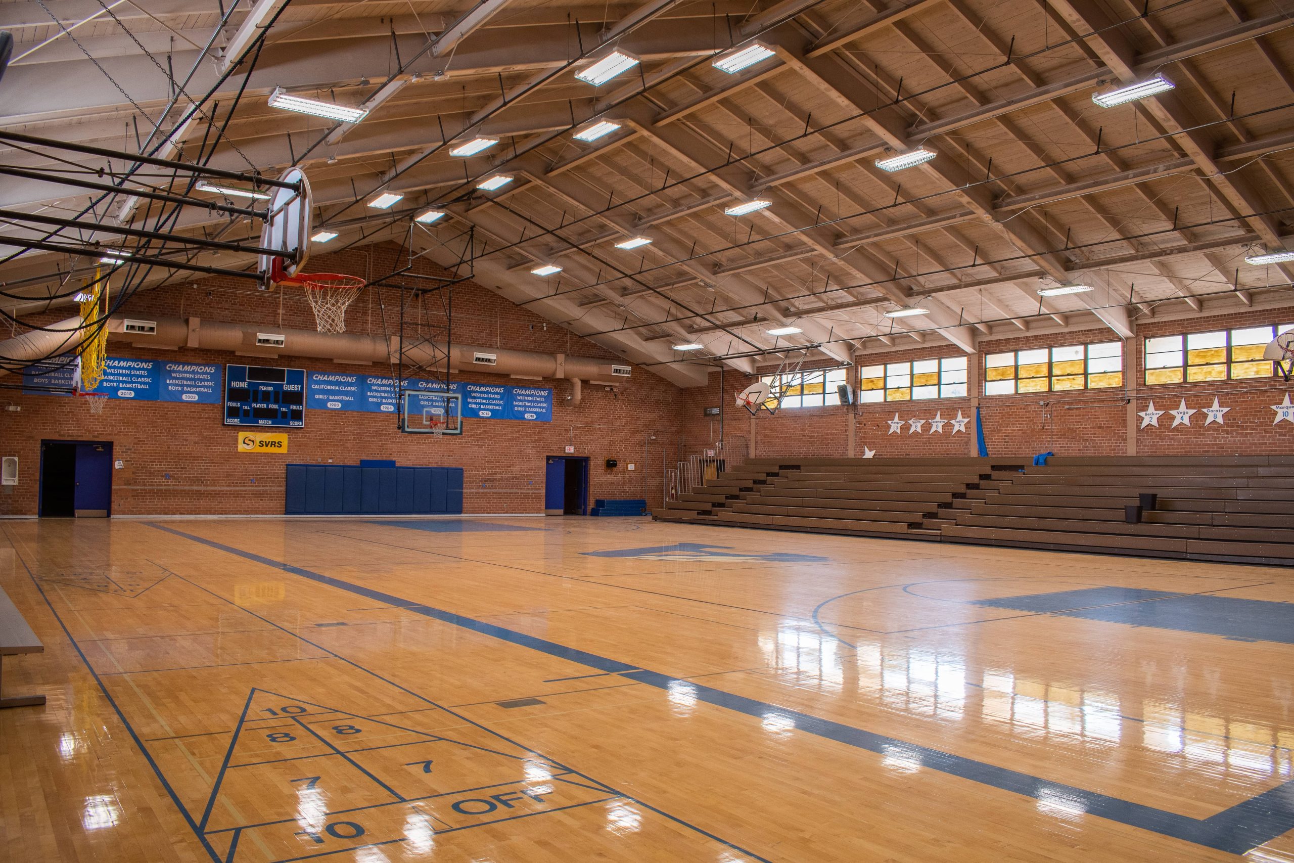 A panoramic photo of the basketball court in the large, ASDB gymnasium. The full-size court is illuminated by a series of large, overhead lights.