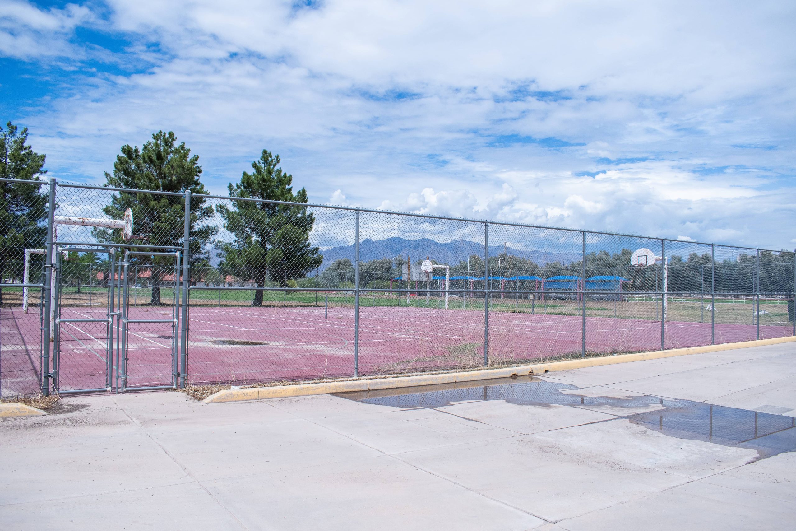 A panoramic photo of the tennis courts on ASDB campus. A tall chain link fence traces the perimeter of the two courts, while a total of four basketball hoops flank them.