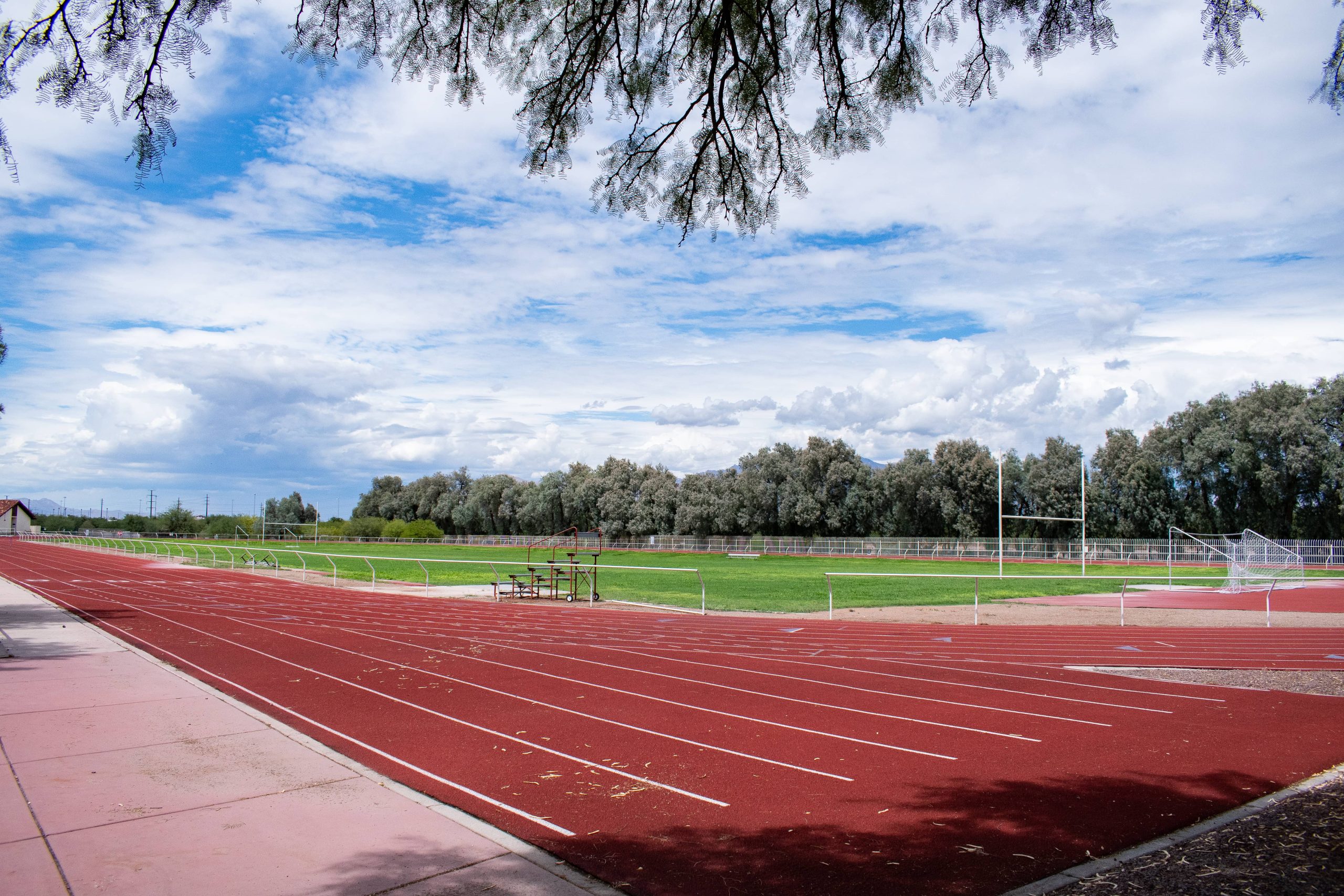 A panoramic photo of the track and field on ASDB campus. The full-size football field and track are flanked on either side by bleachers and a row of large trees.