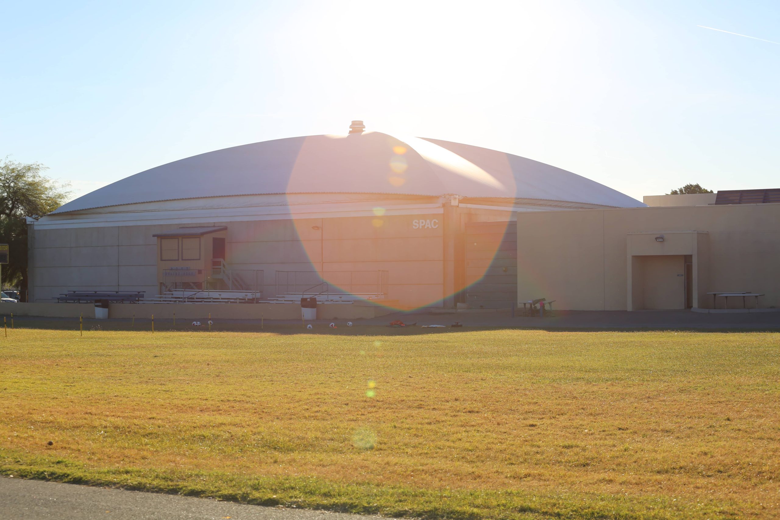 A panoramic photo of the SPAC building on PDSD campus. The large building is pictured in the late afternoon light. Overtop its concrete walls is a large, high strength, tent-like material which functions as the roof of the building.